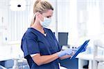 Dentist in mask and blue scrubs using her tablet at the dental clinic