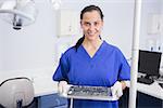 Portrait of a smiling dentist holding tray with equipment in dental clinic