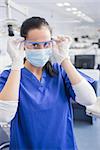 Dentist with surgical mask putting on her safety glasses in dental clinic