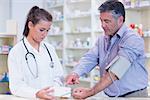 Young trainee taking blood pressure of his customer in the pharmacy