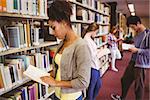 Students reading book against bookshelves in library