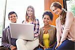 Smiling students sitting on couch using laptop at the university