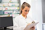 Junior pharmacist writing on clipboard at the hospital pharmacy