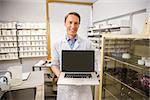 Happy pharmacist showing laptop screen at the hospital pharmacy