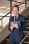 Handsome businessman standing on steps using tablet in office building