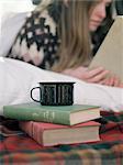 Young woman reading a book, a mug standing on two books.