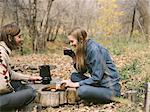 Smiling couple sitting on the ground in a forest, drinking coffee.