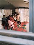 A couple taking a nap in their car, covered by a blanket.