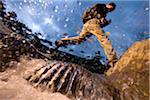 Low angle view of man jumping over a stream while hiking in New Hampshire, USA