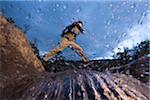 Low angle view of man jumping across river while hiking in New Hampshire, USA