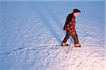 An elderly man walking in the snow using a cane, New England, USA