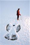 An elderly using a cane, standing in the snow beside a snow angel, New England, USA
