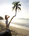 Woman standing on palm tree on beach with sun, Cane Garden Bay, Tortola, Caribbean