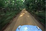 A 1974 VW Beetle drives along a tree-lined road in Pemaquid, Maine, USA