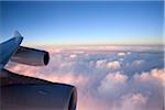 Close-up of the wing and engines of a jet while flying over the clouds at sunset.