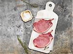 Pork Chops on Parchment Paper and Marble Slab with Salt, Peppercorns and Herbs, Studio Shot