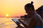 Happy young woman with tablet PC on beach at sunset. Evening sun, sea and beach on background