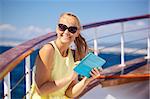 Young smiling woman in sunglasses holding tablet computer and looking somewhere while traveling by ship