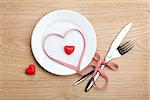 Valentine's Day heart shaped red ribbon over plate with silverware. On wooden table background