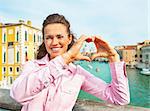 Happy young woman showing heart shaped hands framing santa maria della salute venice, italy
