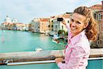 Happy young woman standing on bridge with grand canal view in venice, italy and taking photo