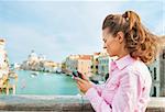 Young woman standing on bridge with grand canal view in venice, italy and checking photos in camera