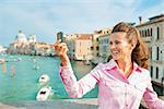 Happy young woman standing on bridge with grand canal view in venice, italy and taking self photo