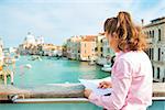 Young woman standing on bridge with grand canal view in venice, italy and looking at map
