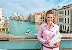 Portrait of happy young woman with map standing on bridge with grand canal view in venice, italy