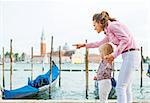 Mother pointing baby on something on grand canal embankment in venice, italy