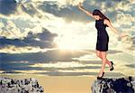 Businesswoman with her arms outstretched as for balance standing on the edge of rock gap and looking down into it. Sky with rays of sunshine through clouds as backdrop