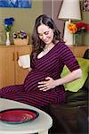 Cute expecting Caucasian woman with mug looking at belly