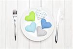 Valentines day toy hearts on plate and silverware. View from above over white wooden table