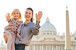 Portrait of happy mother and baby girl waving in front of basilica di san pietro in vatican city state