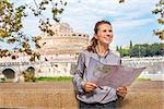 Portrait of happy young woman with map examining attractions on embankment near castel sant'angelo in rome italy