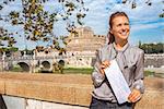Portrait of smiling young woman with map on embankment near castel sant'angelo in rome italy