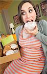 Happy pregnant woman making a mess eating donuts