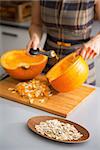 Closeup on seeds and young housewife removing filling from pumpkin in background