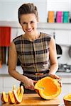 Portrait of smiling young housewife cutting pumpkin in kitchen