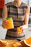 Closeup on young housewife showing jar of pickled pumpkin and pumpkin slices