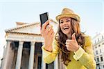 Closeup on happy young woman making selfie and showing thumbs up in front of pantheon in rome, italy