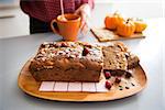 Closeup on freshly baked pumpkin bread with seeds and young housewife making tea in background