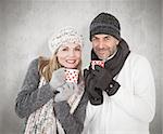 Happy couple in winter fashion holding mugs against weathered surface