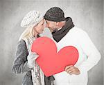 Smiling couple in winter fashion posing with heart shape against weathered surface