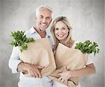 Happy couple carrying paper grocery bags against weathered surface