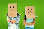 Young couple wearing sad face boxes over head against green vignette
