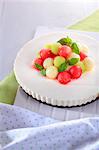 A cream cheesecake decorated with colourful melon balls and peppermint leaves