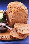 A loaf of bread with brewers grains, two slices cut off, next to butter and jam