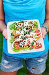 A woman holding a plate of Greek salad