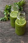 Green smoothies on a wooden table with a bunch of parsley in the background